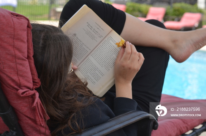 woman sitting in a lounge chair by the pool reading and relaxing on vacation break