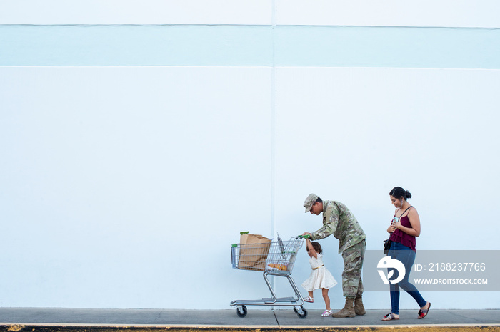 Soldier helping his daughter push a shopping cart