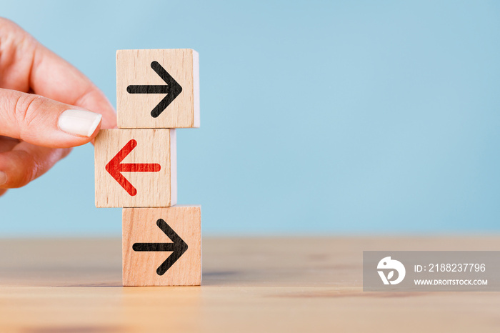 Woman hand holding wooden block with red arrow facing the opposite direction black arrows