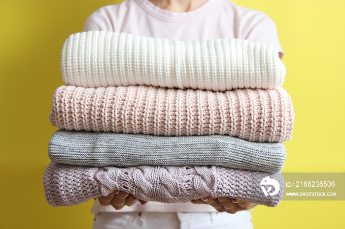 a stack of sweaters in women’s hands on a colored background