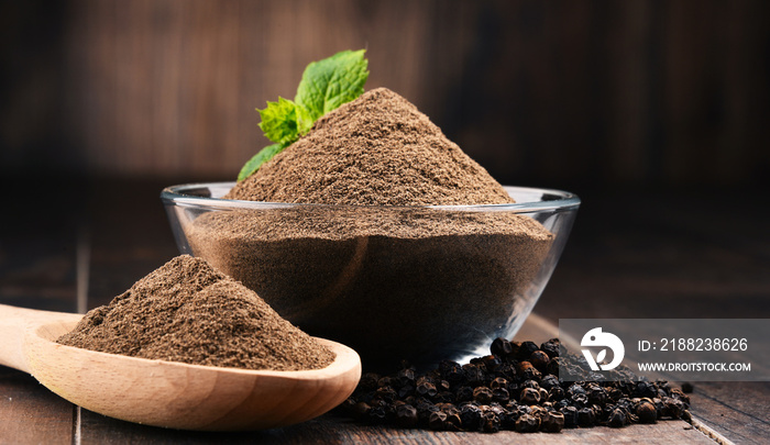 Composition with bowl of ground black pepper on wooden table