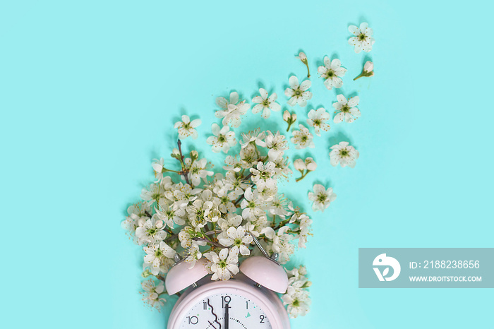 Pink alarm clock and delicate little white flowers on blue background. Top view. Time for love and greetings. Spring Time Change, Spring flowers and Alarm Clock.