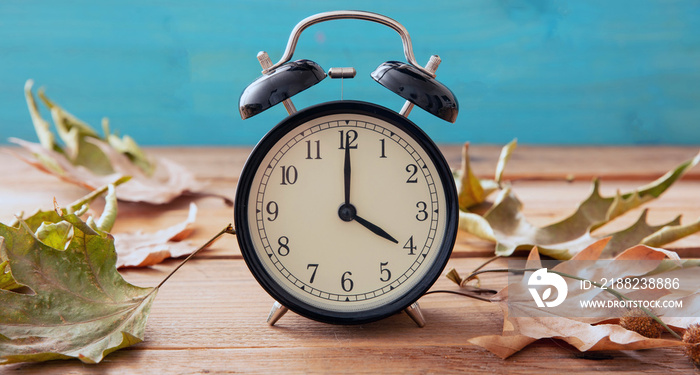 Fall Back Daylight Saving Time. Black clock and autumn leaves on wood