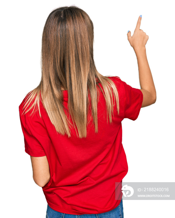 Teenager caucasian girl wearing casual red t shirt posing backwards pointing ahead with finger hand