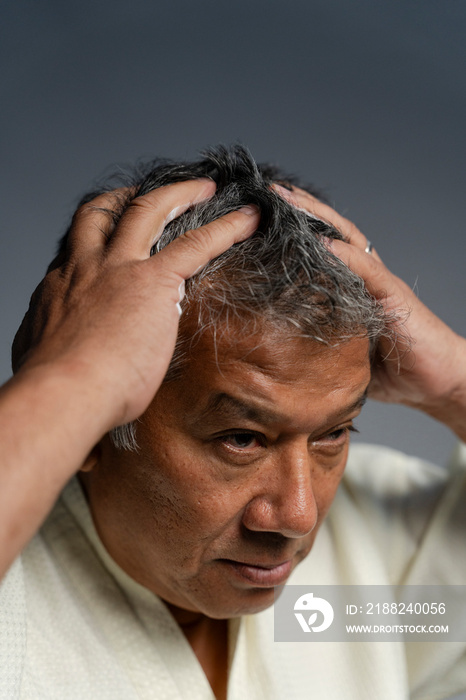 Portrait of man applying hair gel against gray background