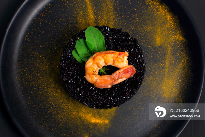 Black rice risotto with Shrimp and safron in a black plate seen from above in dark background close