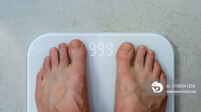 Feet of an obese man standing barefoot on a bathroom scale - view from above the feet