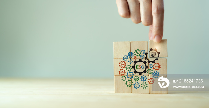 ESG concept of environmental, social and governance. Sustainable corporation development. Hand holds wooden cubes with ESG target icon  standing with other ESG icons on grey background. Copy space.