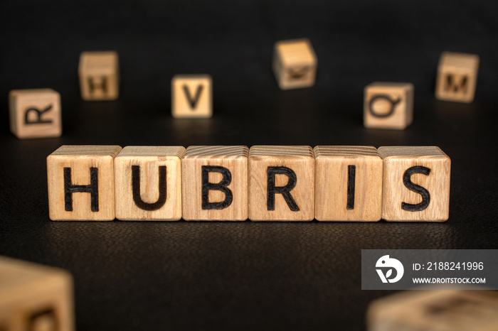 Hubris - word from wooden blocks with letters, excessive pride or self-confidence concept, random letters around black Leather background