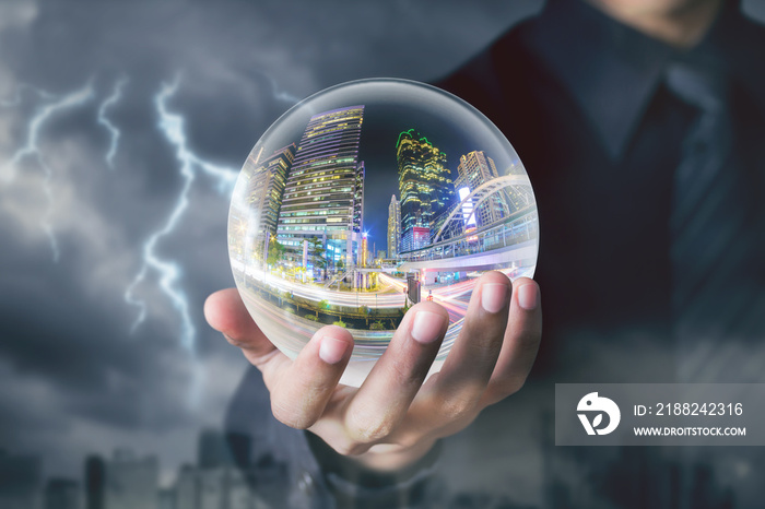 businessman hand hold crystal ball with city night inside with storm and lightning background