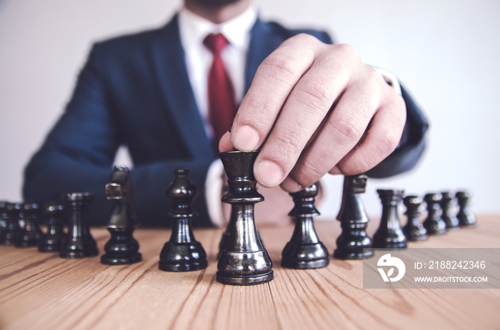 Retro style image of a businessman with clasped hands planning strategy with chess figures on an old wooden table.