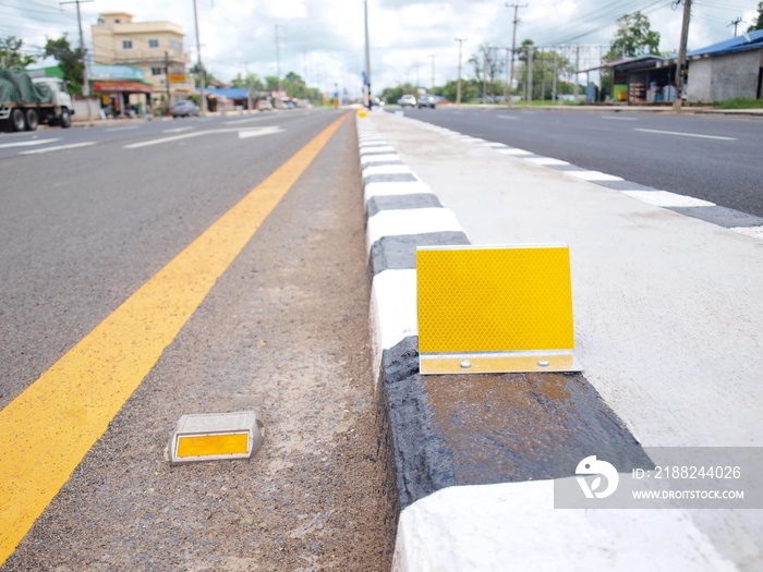 Reflector on median strip. Yellow road markings and concrete curb dividers to increase the safety of traffic on the road. On the background of buildings and blue sky. Selective focus