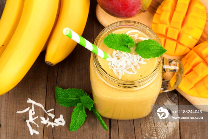 Mango, banana, coconut smoothie in a mason jar glass, overhead view on a rustic wood background