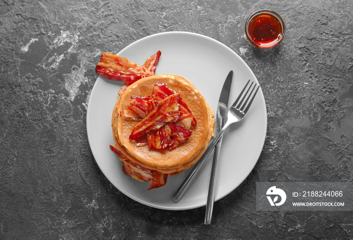 Plate with tasty pancakes and bacon on grey table