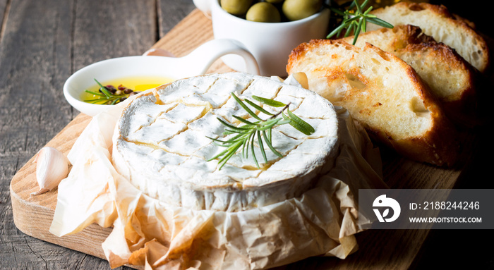 Baked camembert cheese. Fresh Brie cheese and a slice on a wooden board with nuts, honey, rosemary, baguette bread grilled toasts and leaves. Brie type of cheese. Italian, French cheese.