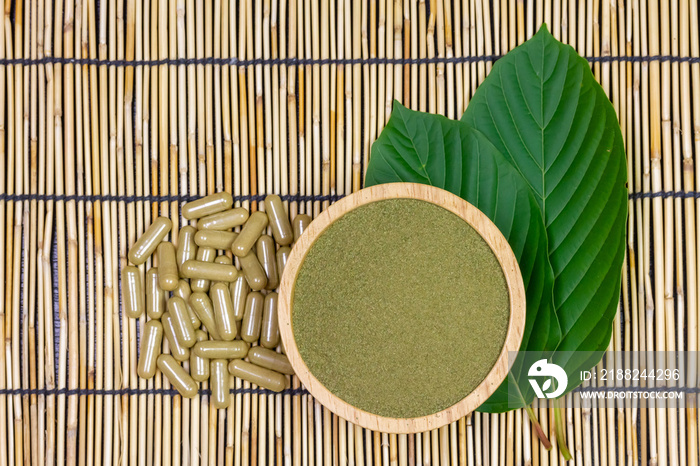 Mitragyna Speciosa Korth or kratom powder on wooden bowl wtih capsules and green leaf on wooden mat, top view and copy space.