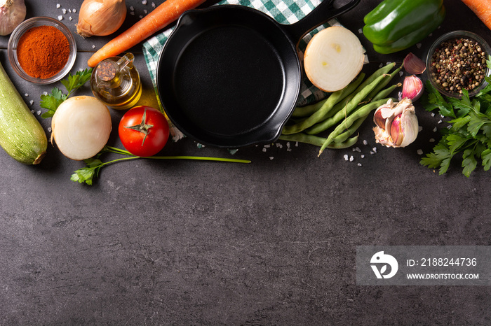 Assortment of vegetables, herbs and spices with iron pan on black background. Top view. Copy space