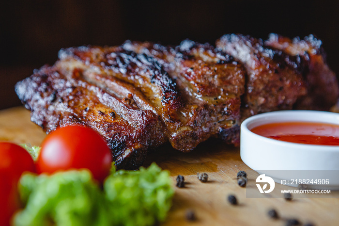 close up of a hearty and juicy piece of fried pork ribs with meat on the bone served on a wooden board with tomatoes and sauce for serving in a meat restaurant