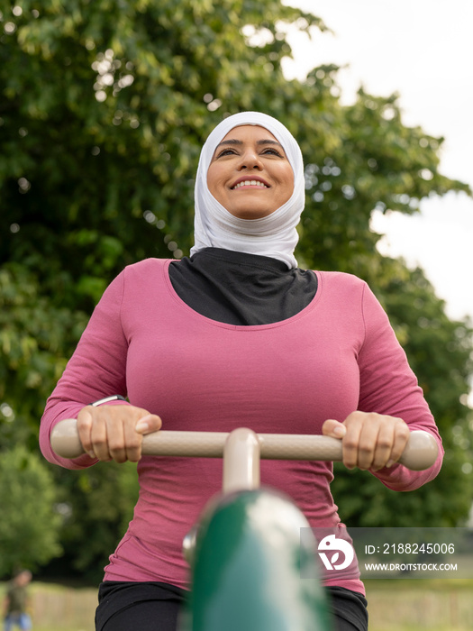 UK,Sutton,Smiling woman in headscarf exercising at park gym