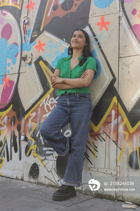 Smiling young woman leaning against of graffiti wall