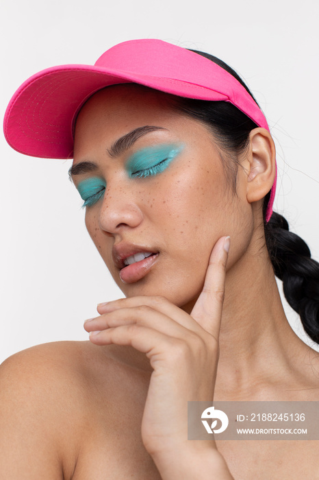 Portrait of woman with closed eyes, wearing blue makeup and sun visor