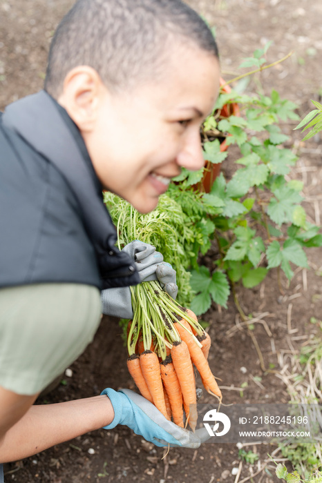 Smiling woman holding bunch of carrots in urban garden