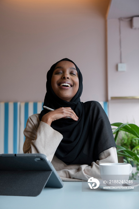 Smiling young woman in hijab working on tablet in cafe