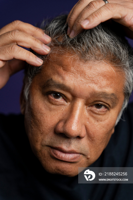 Portrait of serious man styling hair against purple background