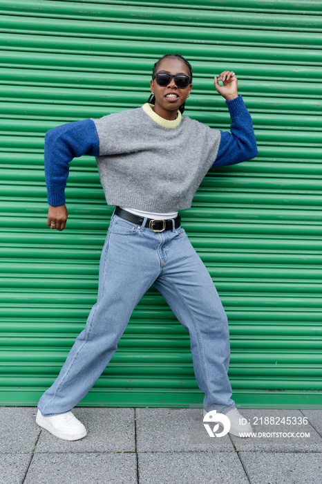 Young stylish woman doing dance pose against green door