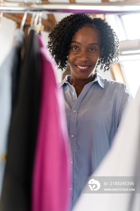 Portrait of fashion designer standing behind clothes rack