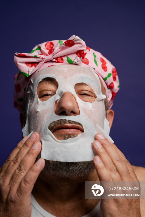 Portrait of man in hair cap applying facial mask against purple background