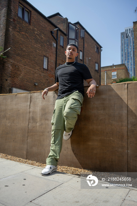 Man wearing back tshirt and cargo pants leaning on wall