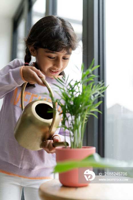 Little girl watering plant at home