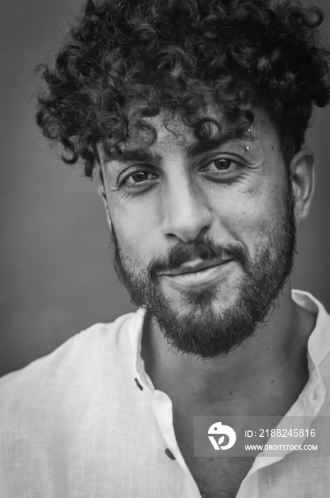 black and white portrait of a young man with beard and curly hair, who smiles slightly while looking at the camera