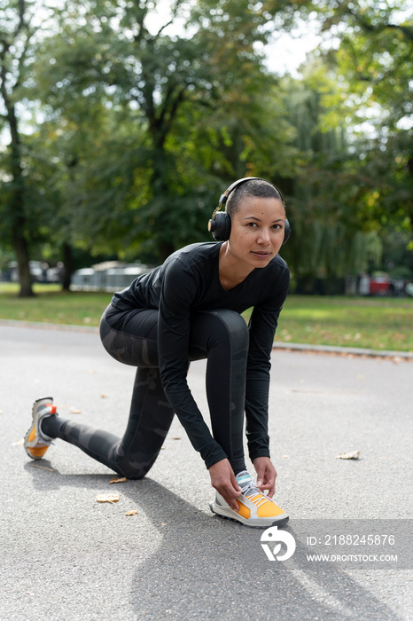 Portrait of woman in sports clothing and headphones tying shoe in park