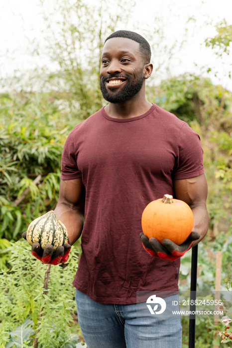 Portrait of smiling man holding pumpkins in urban garden