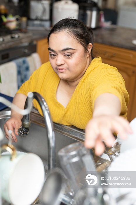 Young woman with down syndrome washing dishes at home