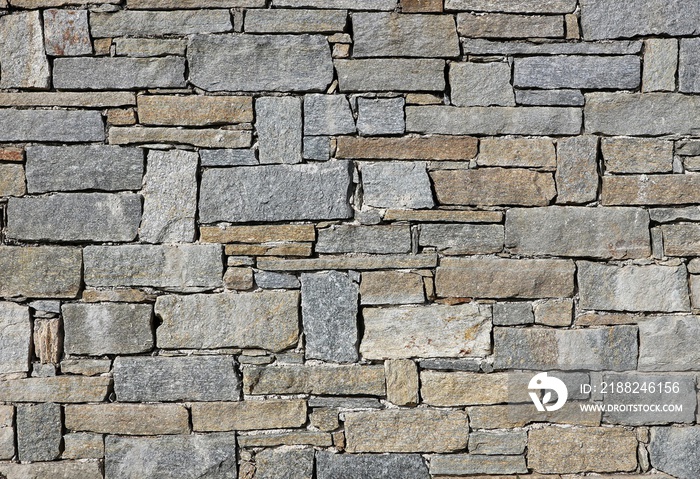 Stone wall made from irregular shaped natural rocks. The colors are gray and brown. Masonry. Background and texture