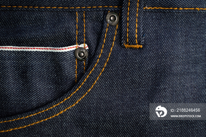 Dark blue jeans texture background with red selvedge pocket and rivets.