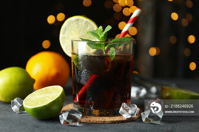 Glass of Cuba Libre on gray textured table against blurred lights