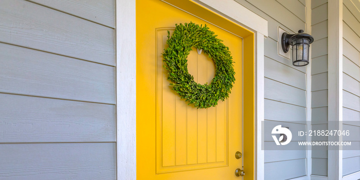 Wreath on yellow front door and a lamp on a wall