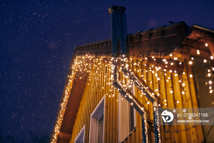 Christmas decorative yellow garlands lights fixed on house roof, outdoor evening Christmas home decoration. Beautiful yellow evening garlands lights on house exterior