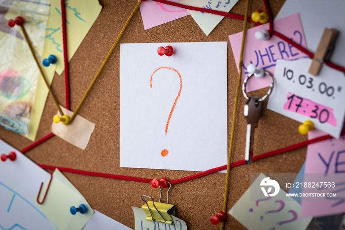 Question concept. Close-up view of a detective board with evidence. In the center is a white sheet attached with a red pin with the question symbol