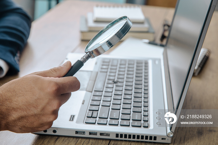 man holding magnifier with laptop