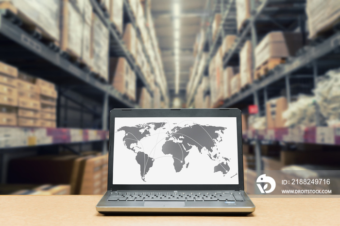 Laptop with white blank screen with global map on brown wooden desk and blurred warehouse store background. Use for cargo Import, Export, Logistics background.