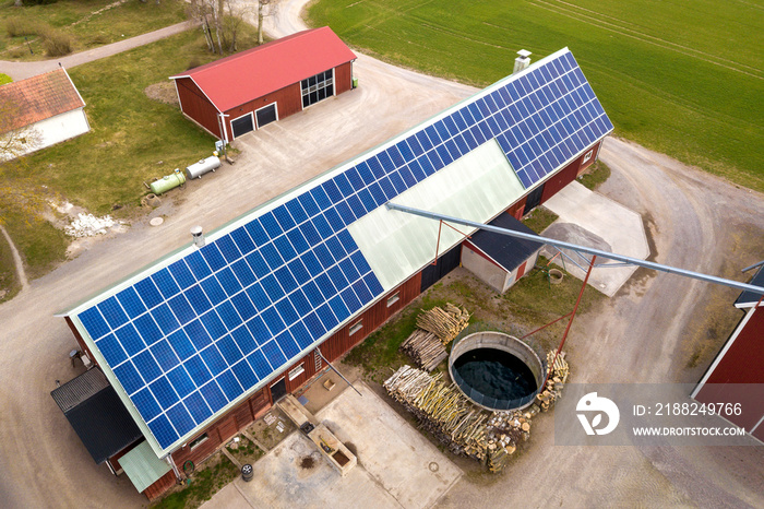 Top view of rural landscape on sunny spring day. Farm with solar photo voltaic panels system on wooden building, barn or house roof. Green field copy space background. Renewable energy production.