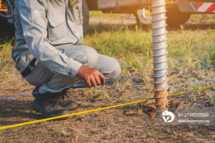 technician installing ground screw for mounting structure of solar panel at solar farm