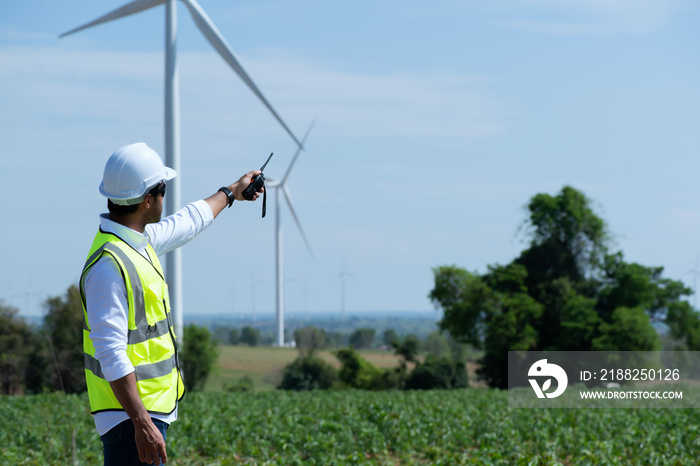 Young  engineer working in wind turbine farm on blue sky background.