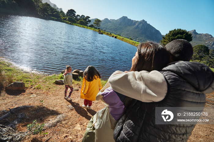 Mom, dad and daughters playing at lake during camping vacation with mountain backdrop and blue sky