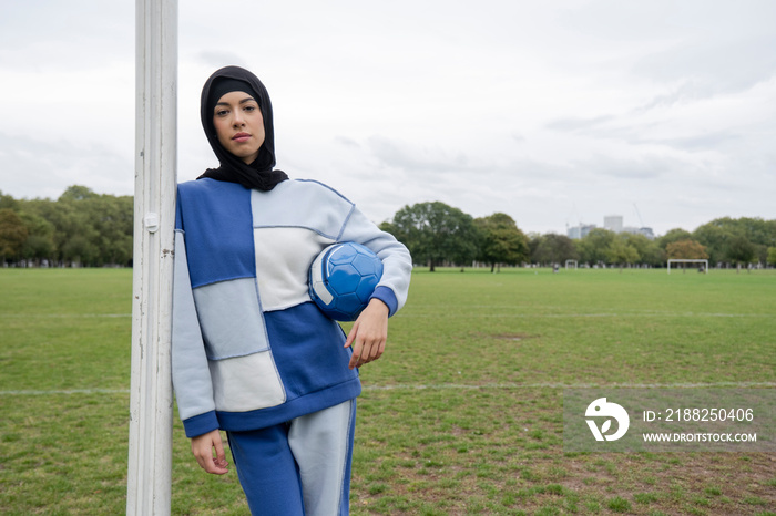 Portrait of woman in hijab standing in soccer field with soccer ball